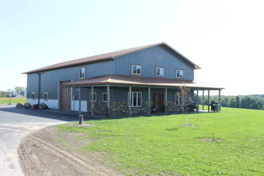 Post-frame building with a wraparound porch and covered outdoor seating area.
