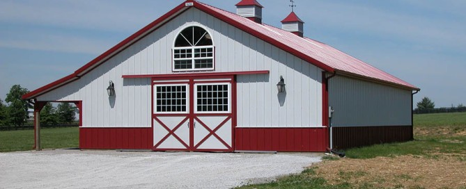 Post-frame pole barn with sliding doors, cupolas, wainscot, and classic barn-style features.