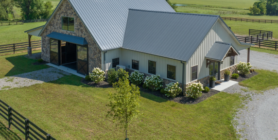 Horse barn with living quarters, stone front, cupolas, fenced paddocks, and covered porch in Kentucky