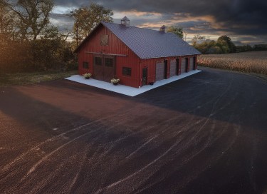 Custom machinery storage building with red steel siding, sliding barn doors, cupolas, and post frame construction in Wisconsin