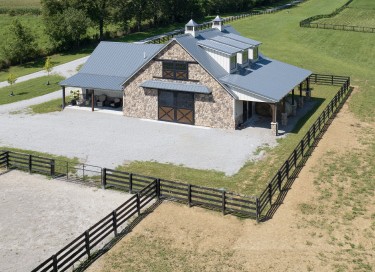 Horse barn with living quarters, stone front, cupolas, fenced paddocks, and covered porch in Kentucky