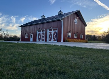 Custom equipment storage building with red steel siding, sliding barn doors, cupolas, and sunset sky in Wisconsin