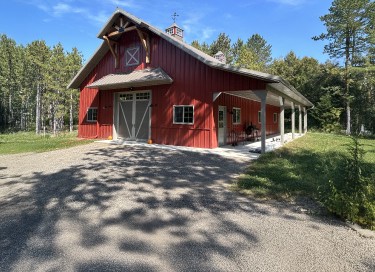 Steel pole barn workshop with red steel siding, covered porch, overhead garage door, and cupola in Wisconsin