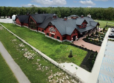 Jeptha Creed Distillery post frame building with red siding, black steel roof, cupolas, and large outdoor patio
