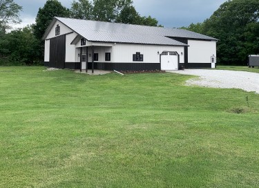 Farm equipment storage building with white steel siding, lean-to addition, sliding barn doors, and gravel drive in Ohio