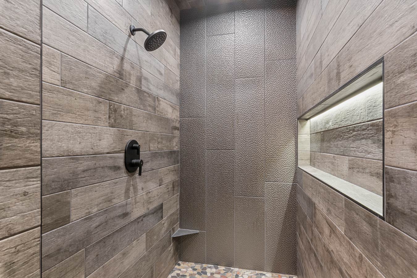 Rustic elegance meets modern design in the custom shower of the Barndominium with Workshop. Featuring textured tiles, a sleek rainfall showerhead, and built-in lighting, this space offers a luxurious retreat with a natural, earthy aesthetic.