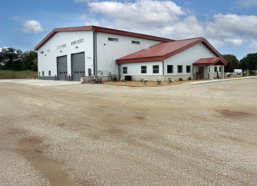 Large industrial steel building with red roof, white siding, overhead service doors, and attached office entrance