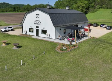 Post frame distillery building with covered patio, cupolas, and black steel roof in rural setting