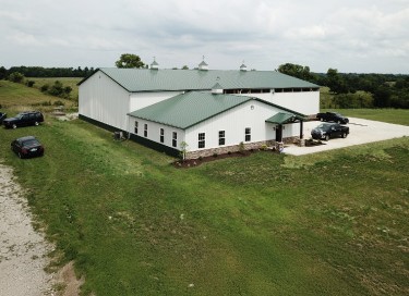Wholesale plumbing warehouse with steel siding, green roof, office space, and overhead doors in rural setting