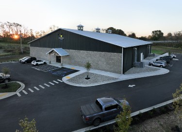 Indoor pickleball facility with stone wainscot, green steel siding, cupolas, and parking lot in Kentucky