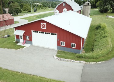 Car collection garage with red steel siding, large overhead door, and rural farm setting with silo in Wisconsin