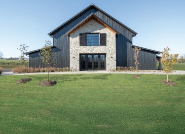 Keene Ranch event barn with black steel siding, stone front entrance, and large glass doors in Kentucky