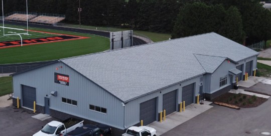 Maintenance garage with steel siding, multiple overhead doors, and attached office near sports field