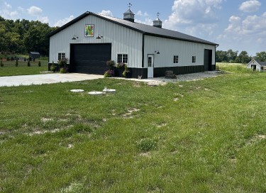 Rural pole barn garage with white steel siding, large overhead door, cupolas, and countryside setting