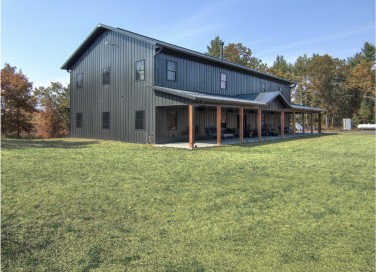 Luxury black barndominium with steel siding, wraparound porch, and wood posts in WisconsinAugusta, Wisconsin