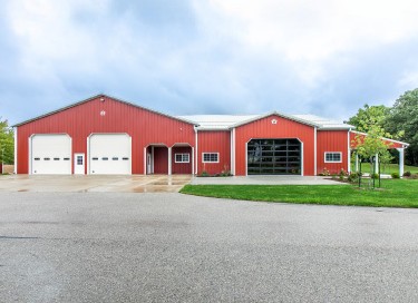 Antique tractor garage with red steel siding, glass overhead door, multiple garage bays, and covered porch in Wisconsin