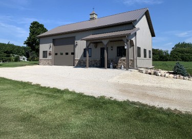 Residential workshop with steel siding, stone wainscot, covered porch, and overhead garage door in Wisconsin