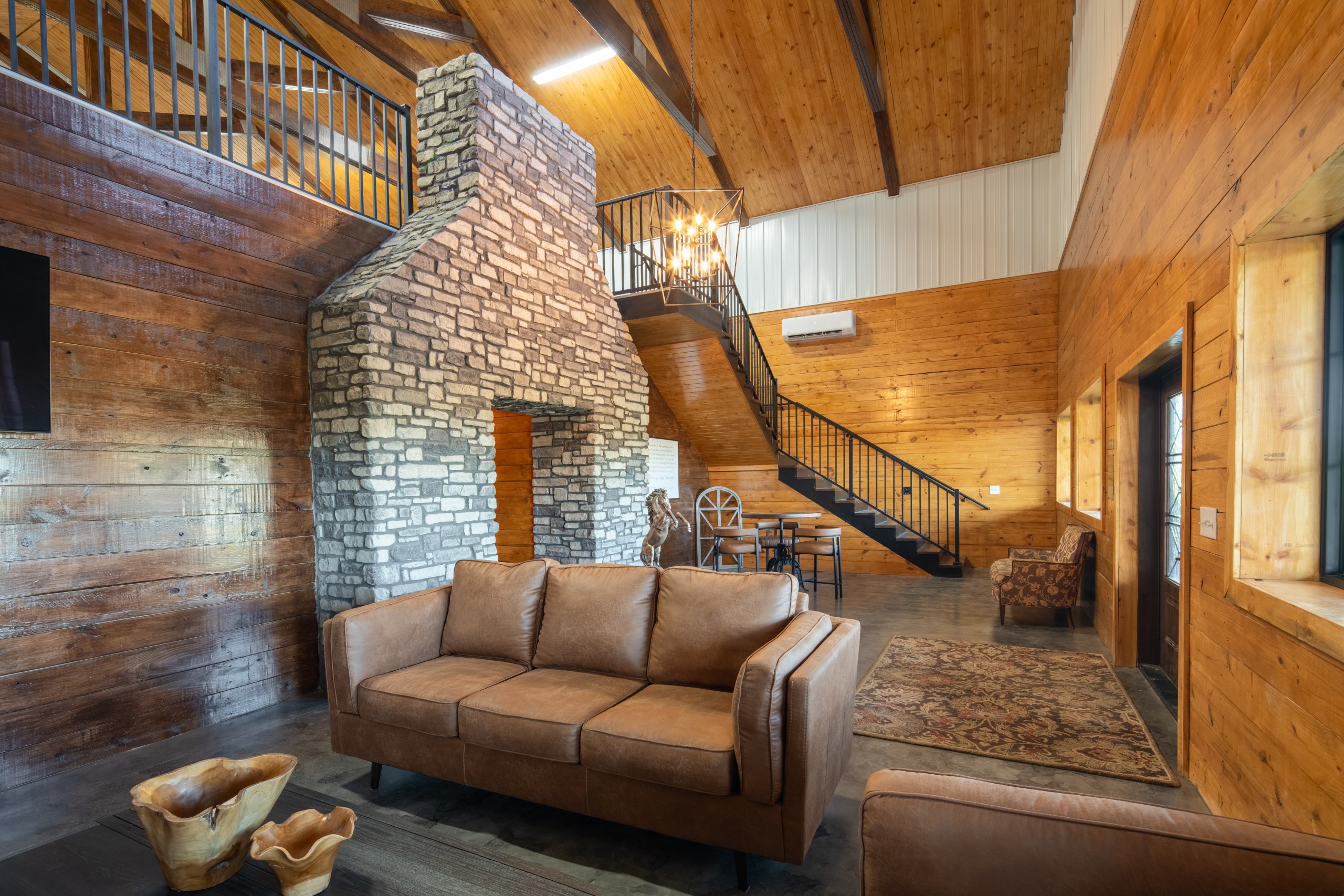 Lobby seating area at The Settlement Equestrian Center with stone feature wall, staircase to loft, and warm wood interior finishes