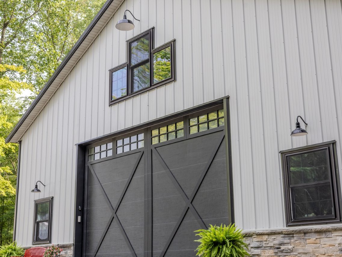 Custom black garage door with windows, stone wainscot and gooseneck lighting on post-frame storage building