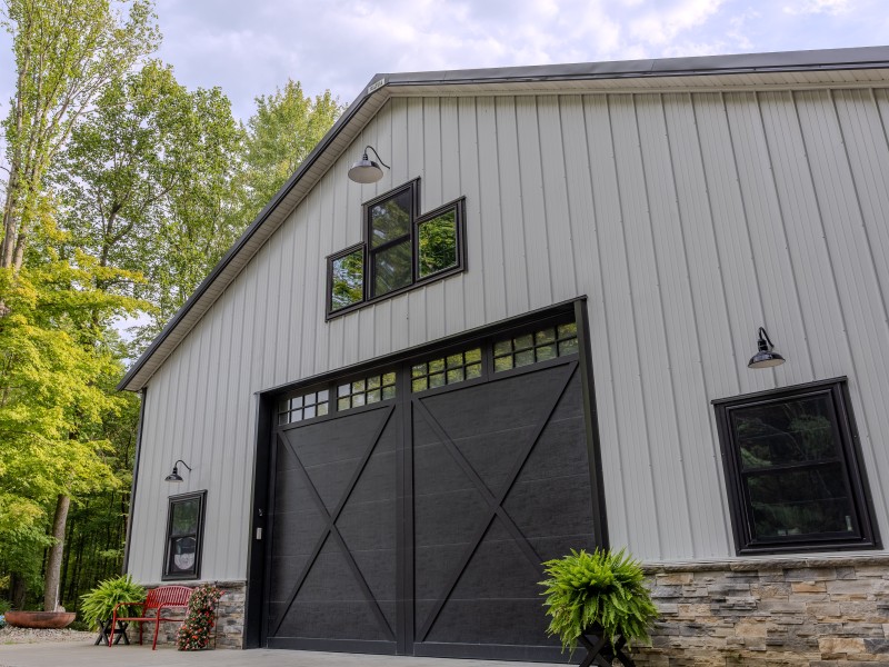 Custom Storage Building Front Elevation – Xenia, Ohio Custom post-frame storage building with stone wainscot, black overhead door, gable windows and gooseneck lighting