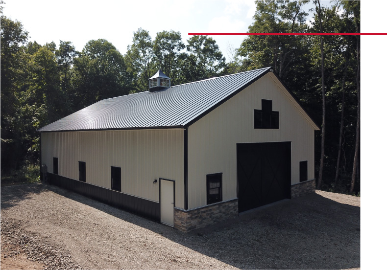 Front view of pole barn with black overhead doors, gable windows, white siding, and stone wainscot accents