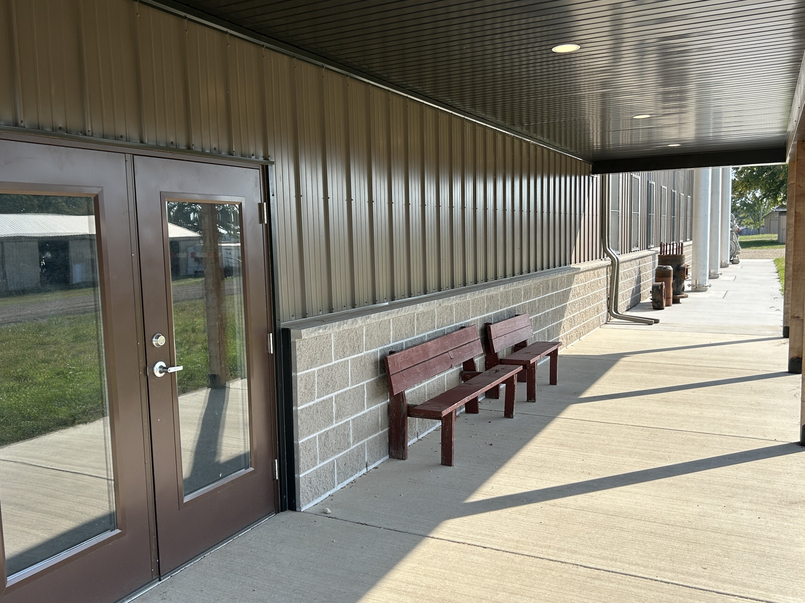 Covered porch at the Baer Powerhouse with dual glass entry doors, bronze steel siding, stone wainscot, and concrete walkway.