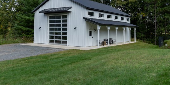 30' x 48' pole barn garage with white steel siding, black roof and trim, covered porch, and custom glass overhead door