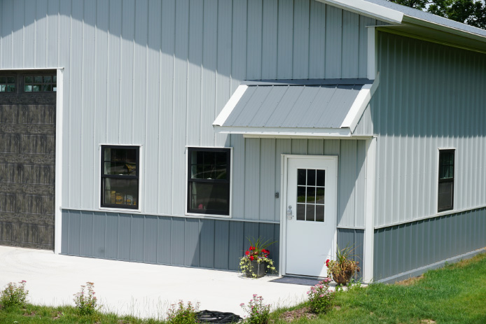 40x60 custom pole barn garage with white steel siding, charcoal wainscot, entry awning, and black windows