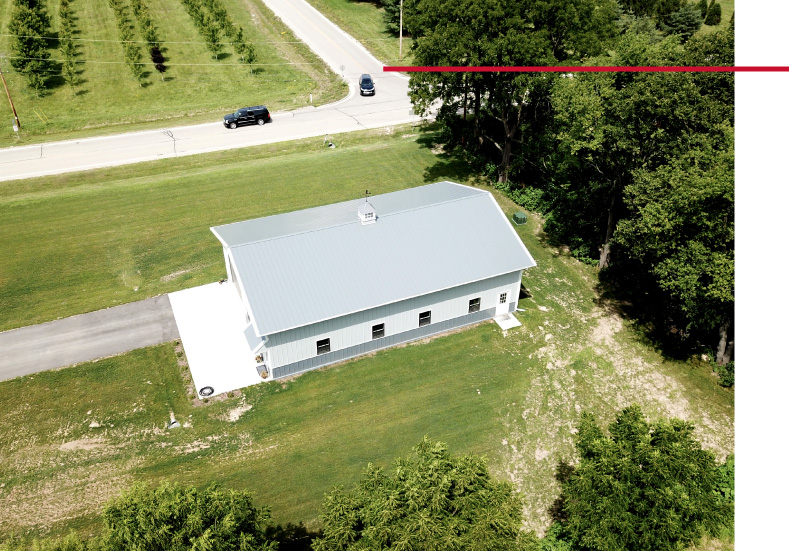 40x60 backyard pole barn garage on acreage with white steel siding shown from aerial drone view