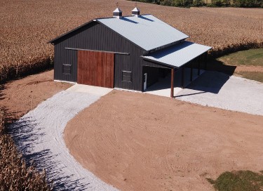 40x64 pole barn garage with black steel siding, wood overhead doors, cupolas, and covered lean-to