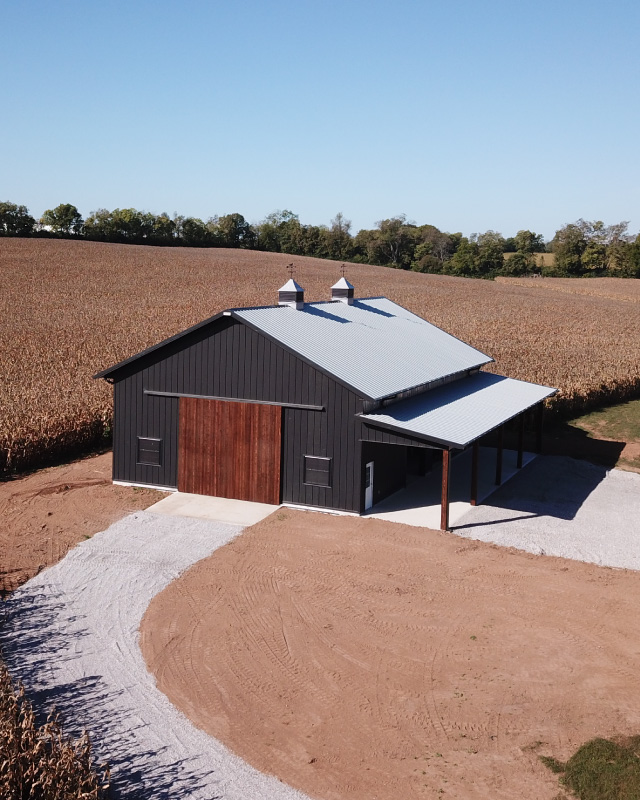 40x64 pole barn with black steel siding, wood sliding doors, cupolas, and covered lean-to