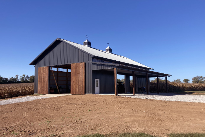 40x64 pole barn with black steel siding, wood sliding barn doors, open bays, and covered lean-to