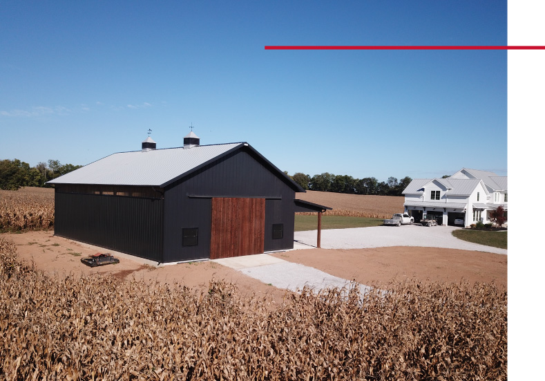 Exterior view of 40x64 pole barn with black siding, wood sliding doors, and lean-to addition in rural residential setting