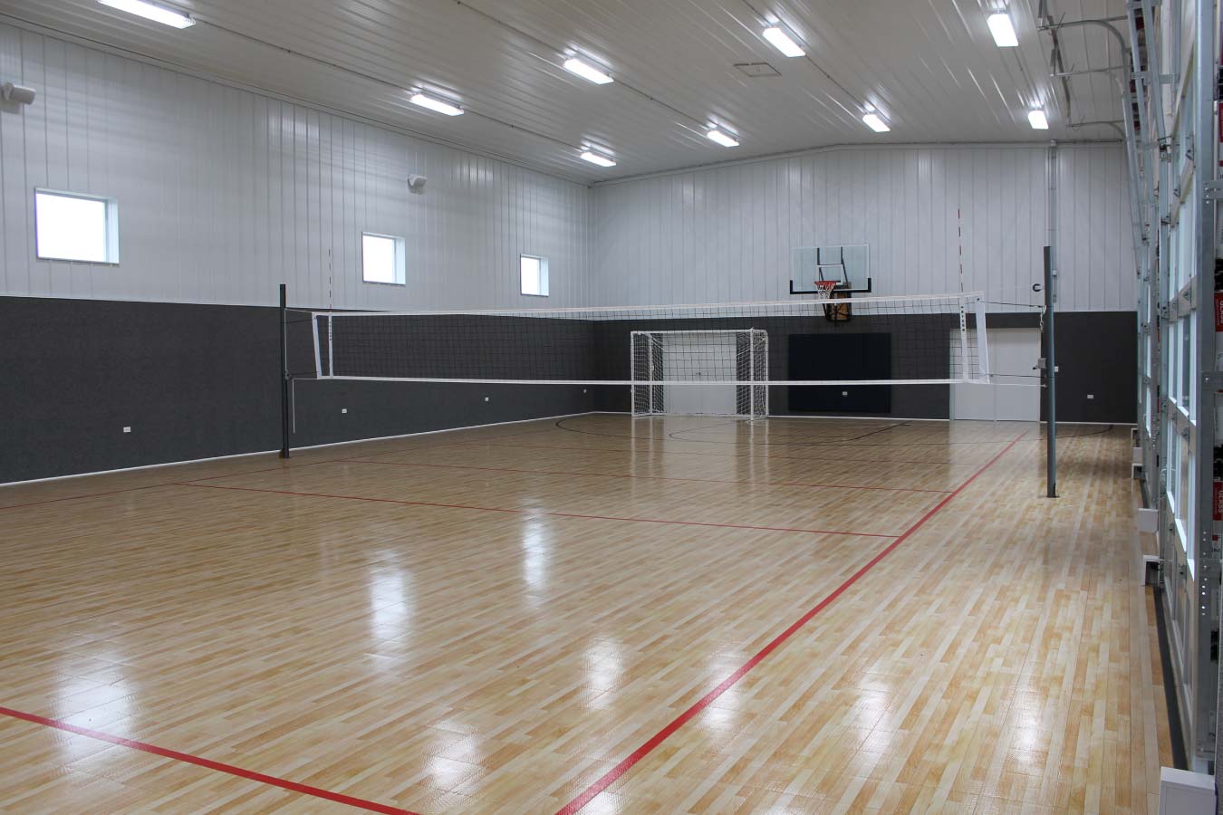 Indoor basketball and volleyball court inside custom post frame sports building with hardwood flooring and clear-span interior
