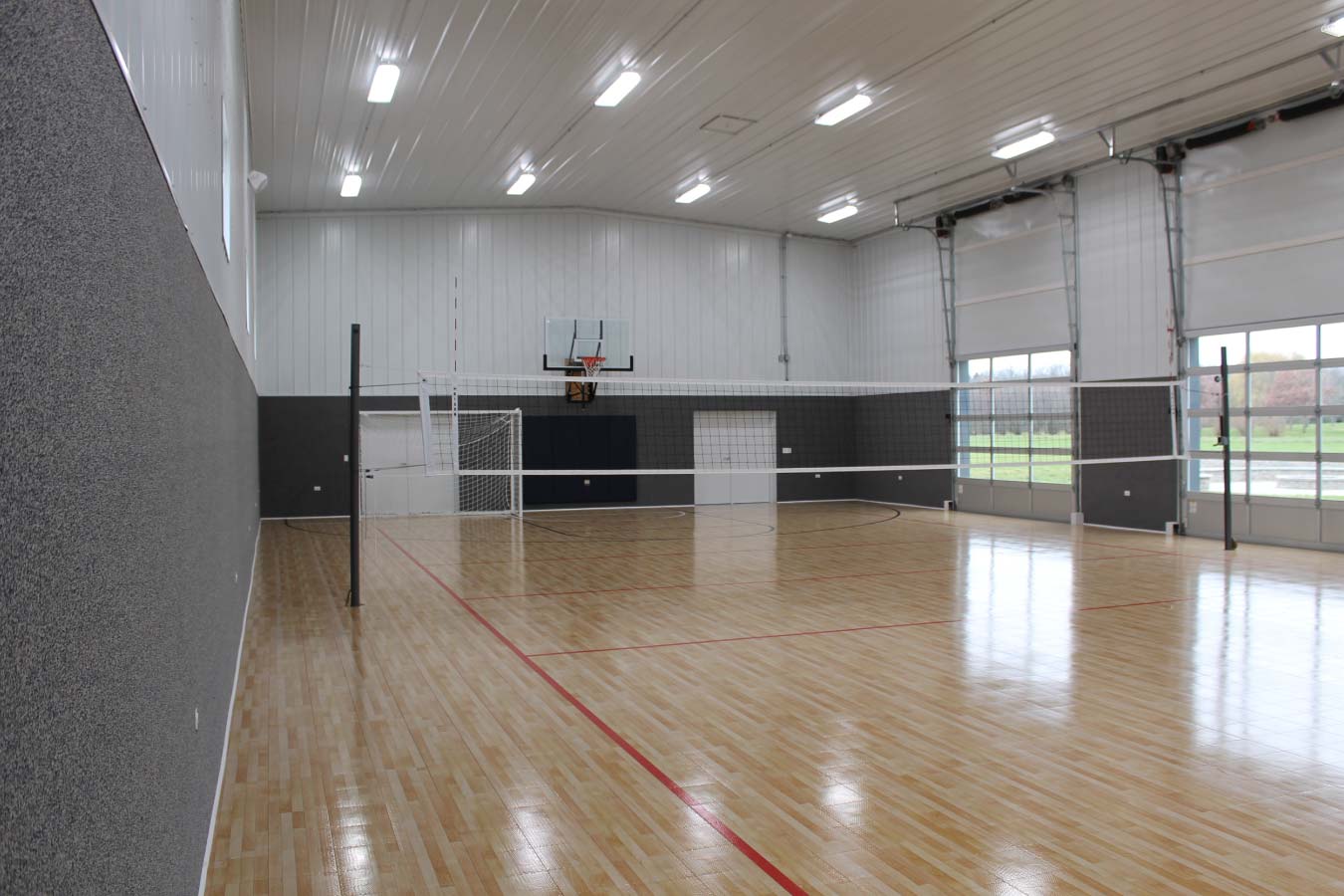 Indoor basketball and volleyball court inside custom post frame sports building with hardwood flooring and clear-span interior