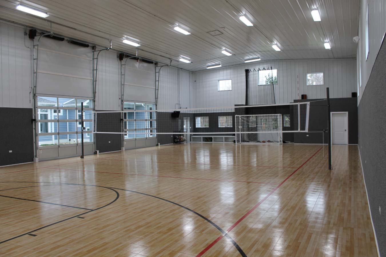 Indoor basketball and volleyball court inside custom post frame sports building with hardwood flooring and clear-span interior