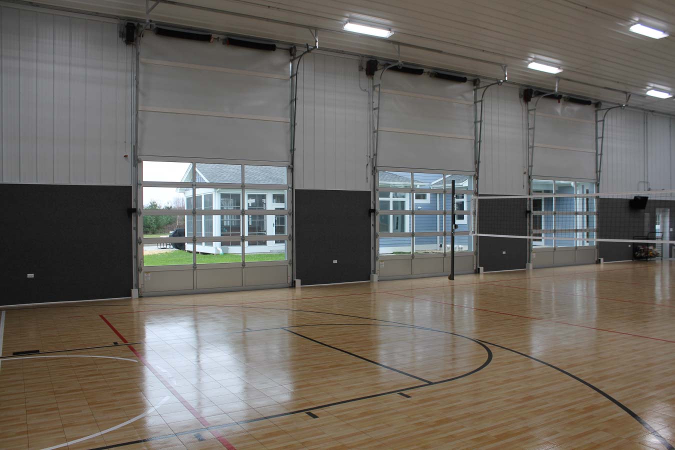 Indoor basketball court with hardwood flooring glass overhead doors and clear-span post frame construction