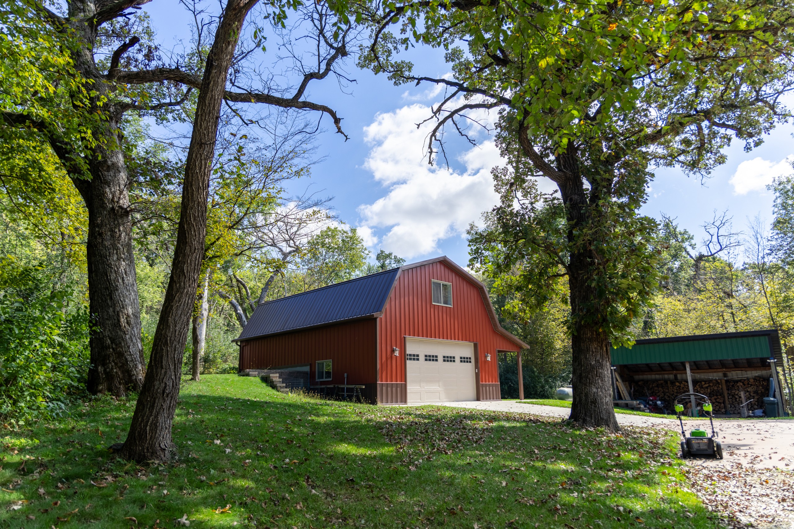 Red steel gambrel garage with a brown roof and trim surrounded by mature trees on a wooded Minnesota property