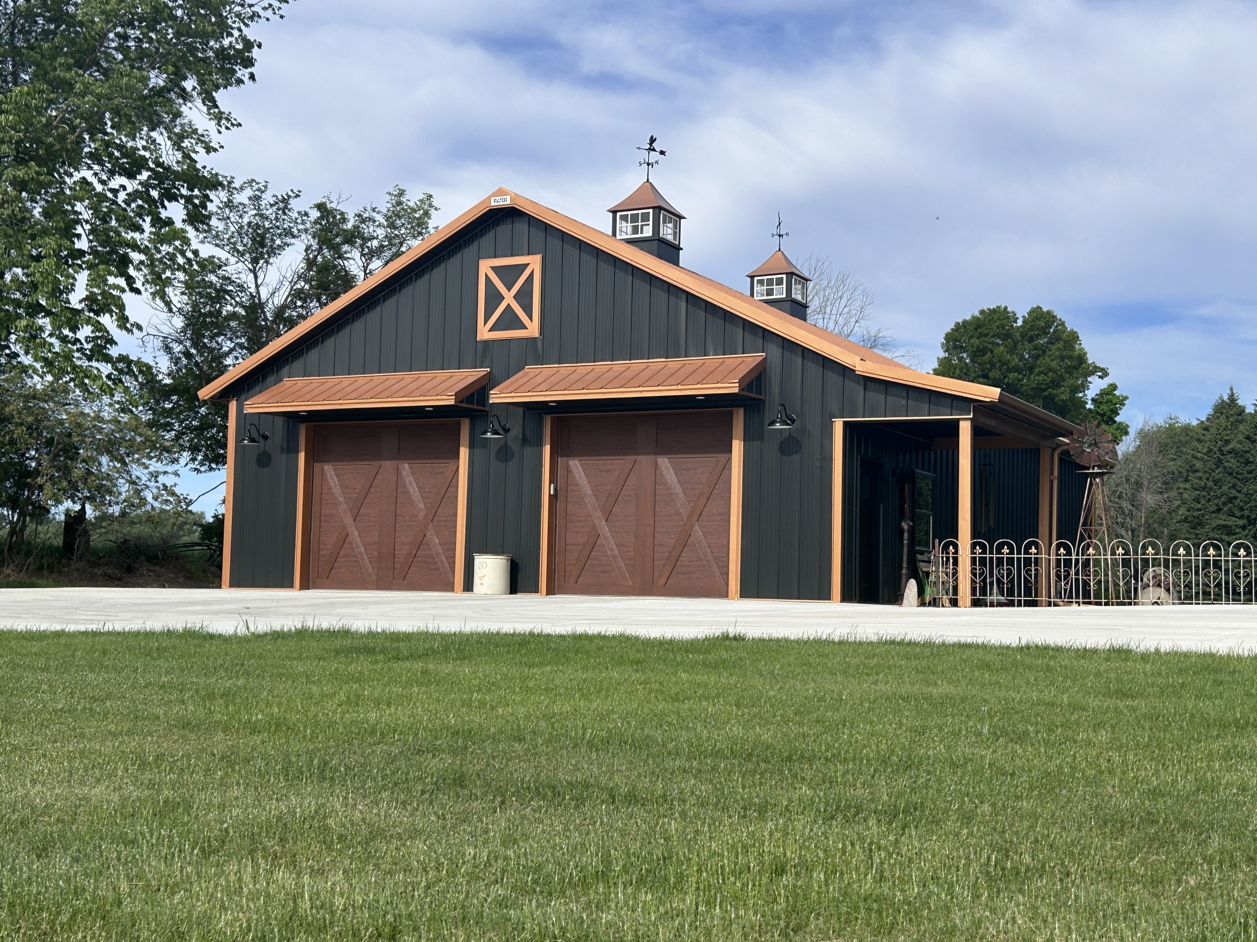 Full view of 36x50 black metal garage with copper roof, copper trim, cupolas, Clopay doors, and side porch by Walters Buildings