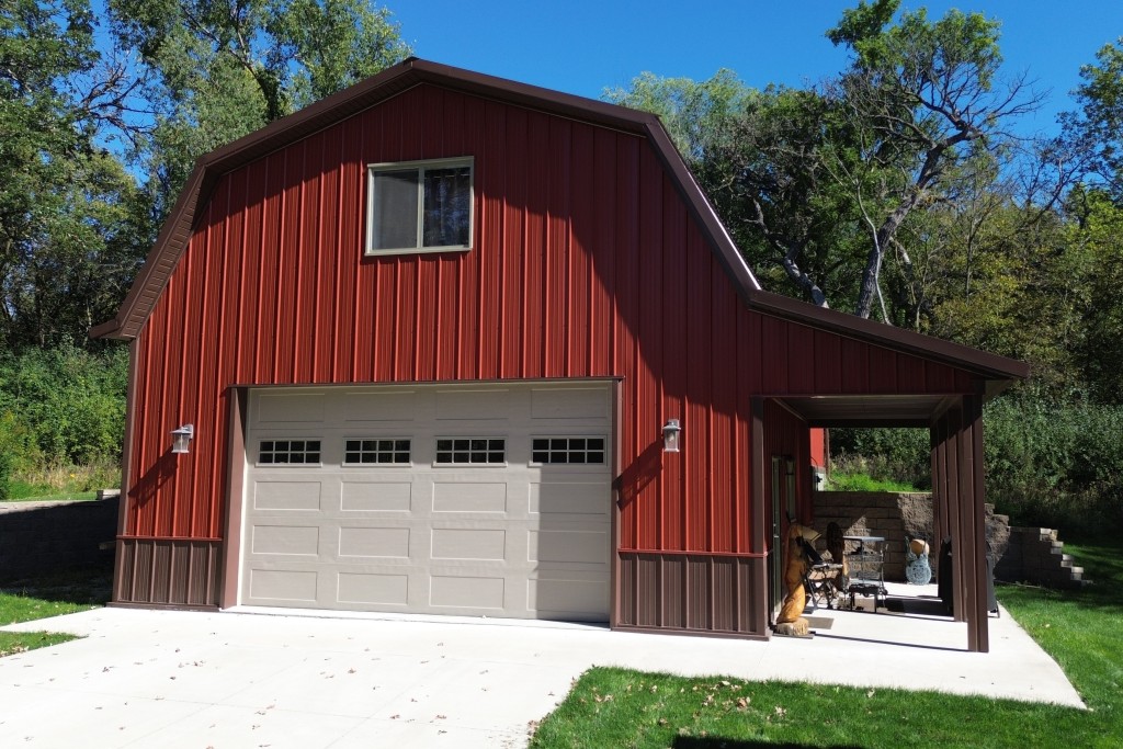 Custom Metal Pole Barn Garage Features Custom metal pole barn garage with a gambrel roof, red steel siding, brown wainscot, overhead door and side porch