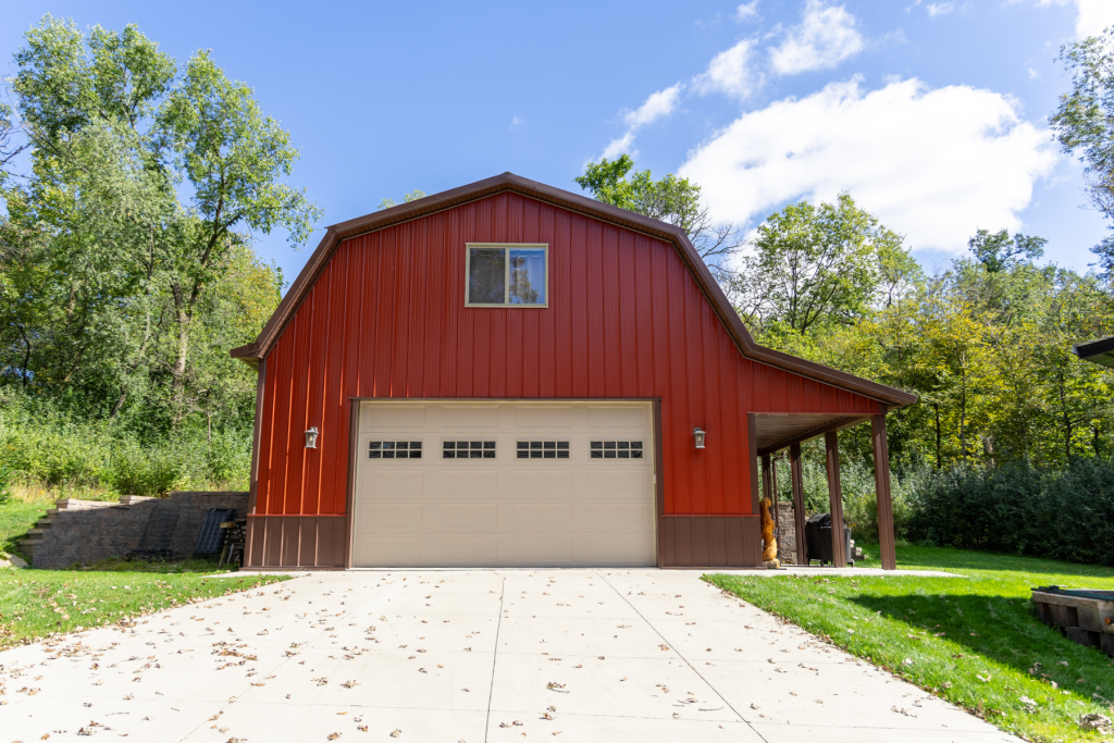 30′ x 40′ Post-Frame Gambrel Garage Front view of a 30' x 40' post-frame gambrel garage with red steel siding, brown trim, an overhead door and a side porch