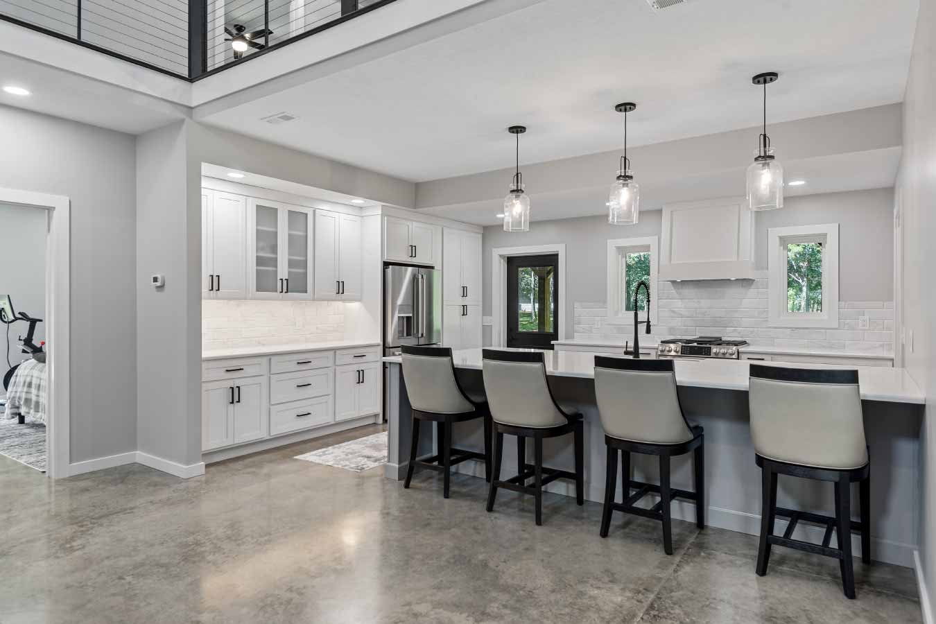 Interior view of a modern post-frame barndominium kitchen featuring polished concrete floors, a large quartz island with bar seating, white shaker cabinets, stainless steel appliances, and pendant glass lighting. The open-concept layout showcases residential-quality finishes in a custom-built barndominium, blending rustic structure with luxury home design.