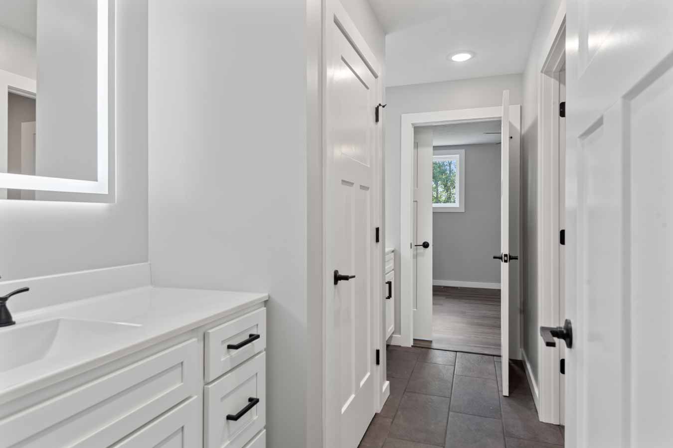 Modern Jack and Jill bathroom in a barndominium with dual vanities, LED mirror, and tile flooring connecting two upstairs bedrooms.