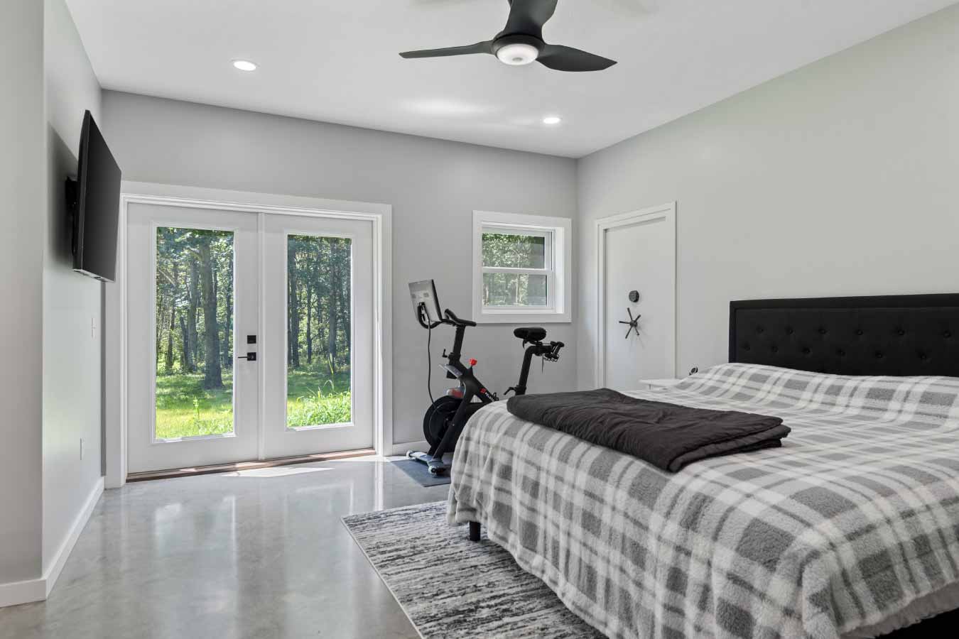 Primary bedroom with polished concrete floors, private patio access, ceiling fan, and secure vault door leading to a gun or safe room.