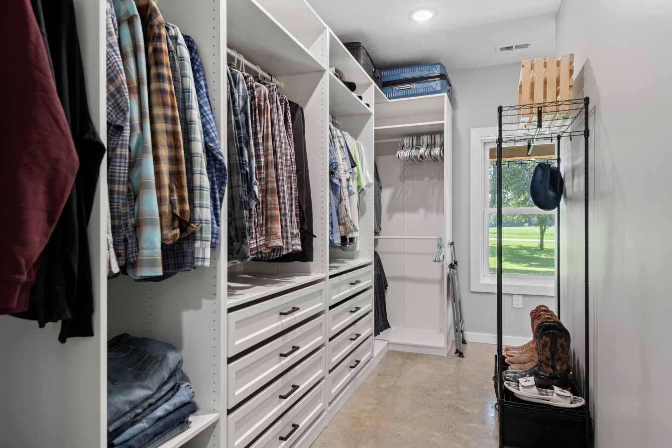 Spacious walk-in closet with custom built-in shelving, multiple hanging rods, and a window offering natural light and a view of the yard.