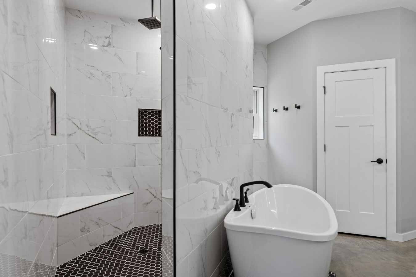 Walk-in shower with rainfall shower head and built-in bench in the master bathroom of a modern barndominium.