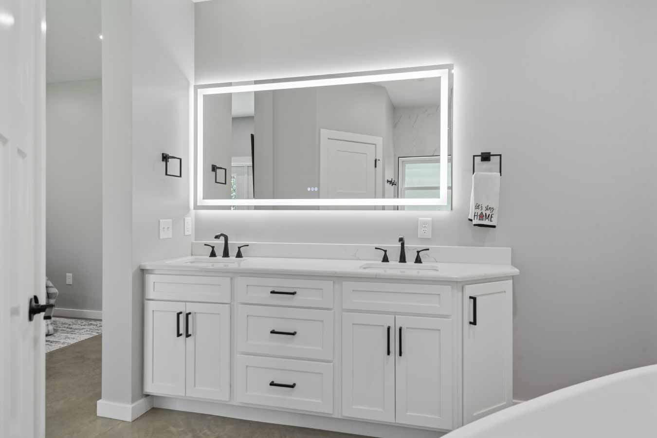 Double vanity with LED mirror in the master bathroom of a modern barndominium.