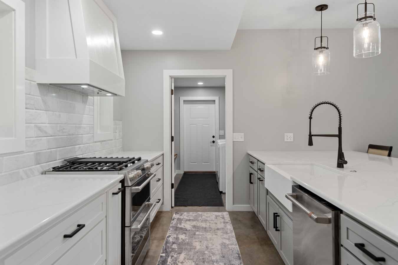 View from the kitchen in a modern barndominium looking toward the mudroom and garage entry, featuring a farmhouse sink and pendant lights.