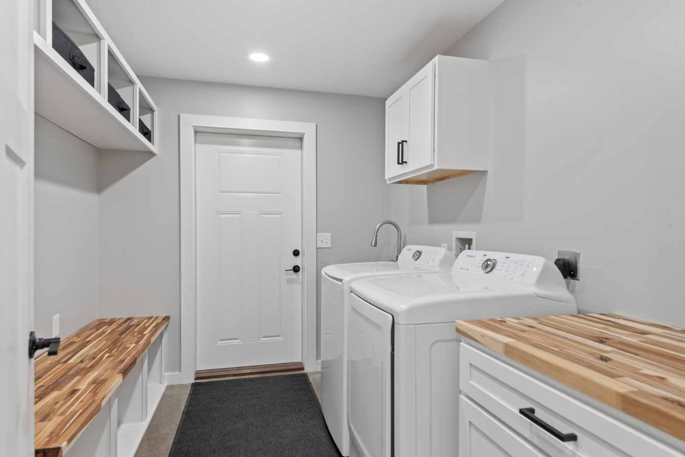 Modern mudroom with built-in bench, laundry area, and entry door from garage in a barndominium.
