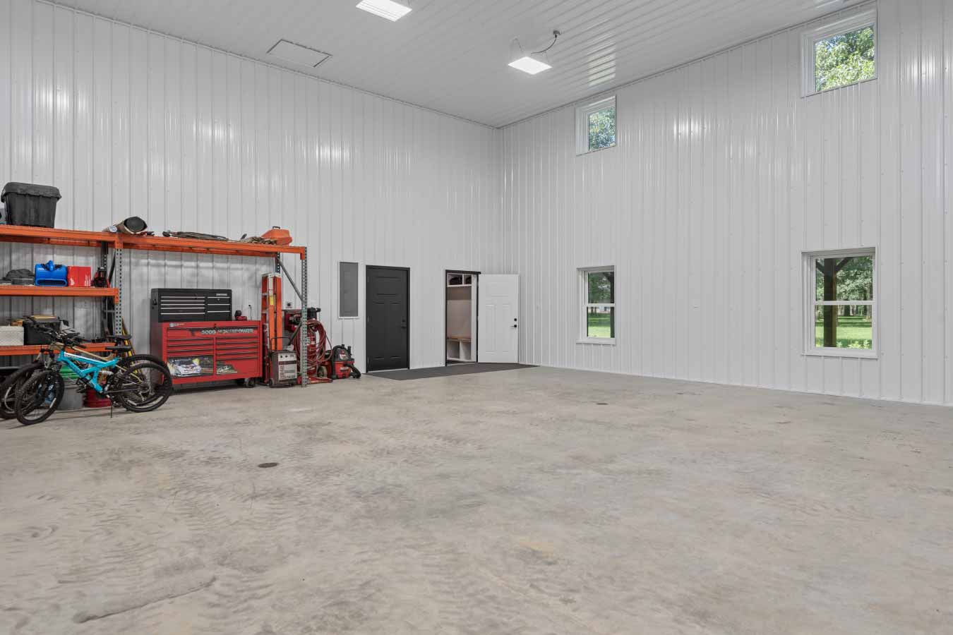 Interior view of a spacious 36' x 36' x 18' insulated garage with in-floor radiant heat, high ceilings, storage shelves, and natural light from multiple windows.